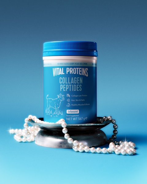 A premium product hero shot featuring a jar of collagen peptides resting on a silver pedestal, adorned with elegant strings of pearls against a soft blue gradient background.
